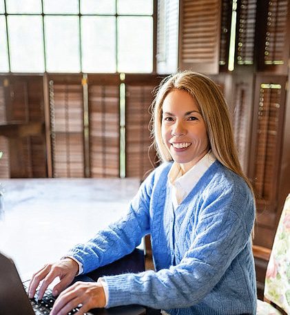 Smiling woman working on laptop in sunlit room